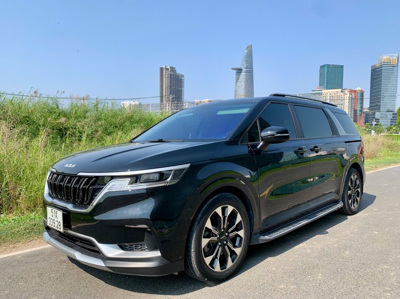 Xe Kia Carnival VIP màu đen tại TP.HCM, phía sau là các toà nhà trung tâm Quận 1